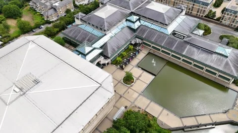 Angular grey roofs and glazed ridges of a large modernist building step down to Stock Footage 343469391