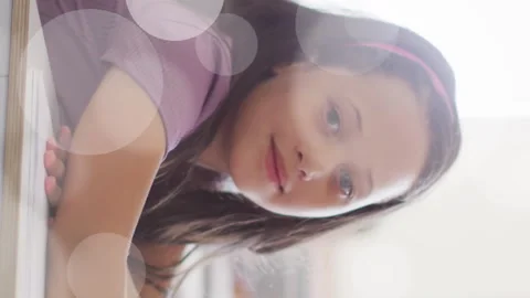 Animation of bokeh light spots over happy schoolgirl sitting at desk in class Stock Footage 312504636