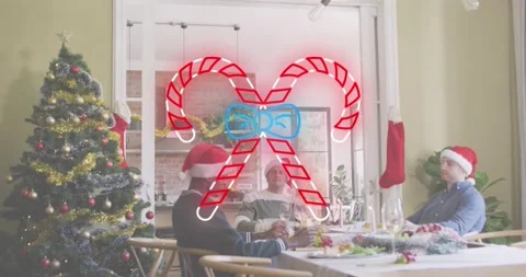 Animation of candy cane icon over diverse friends sitting at table at christmas Stock Footage 210222334