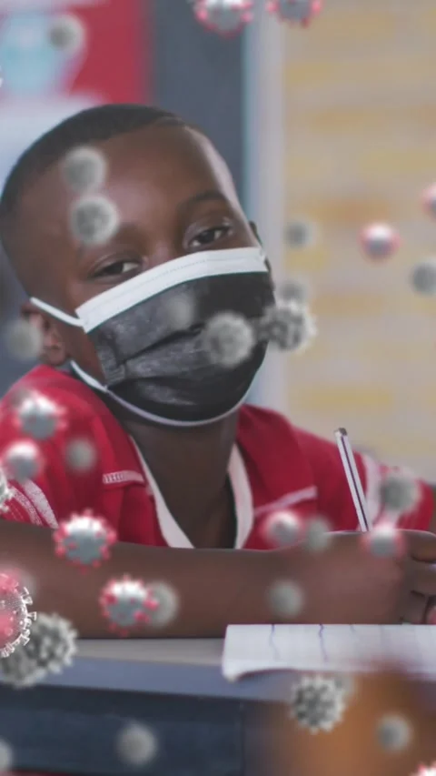 Animation of covid 19 cells floating over schoolboy in face mask in classroom Stock Footage 342225412