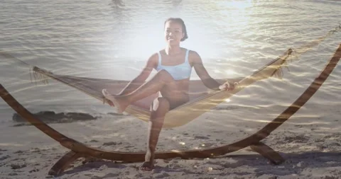 Animation of light over happy african american woman in hammock on beach 库存影片 201964573