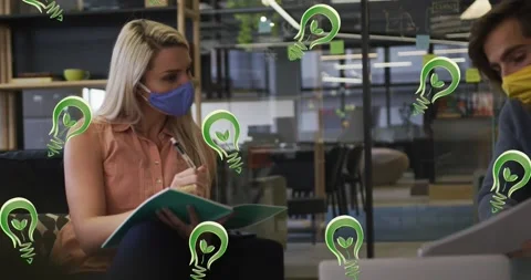 Animation of lightbulb icons over diverse business people wearing face masks and Stock Footage 161454941