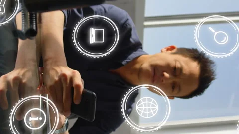 Animation of multiple icons over asian man sitting on chair and scrolling on Stock Footage 313412027