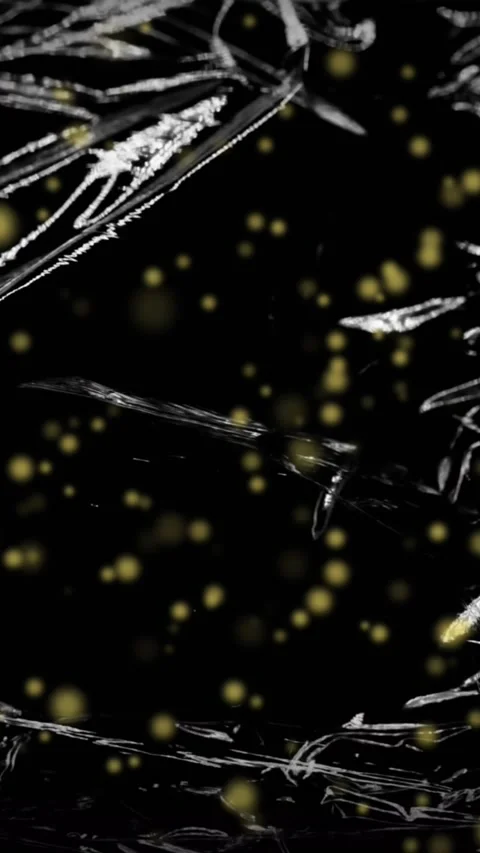 Animation of yellow particles floating over light on moving shiny black plastic Stock Footage 323922445