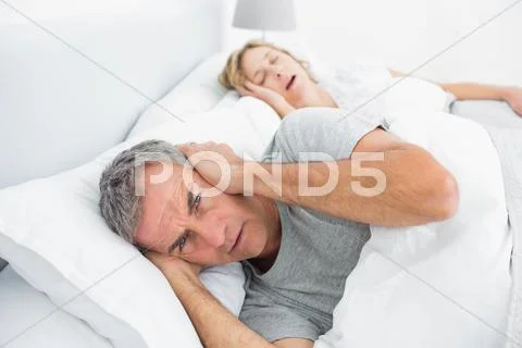 Annoyed man blocking his ears from noise of wife snoring Stock Photos