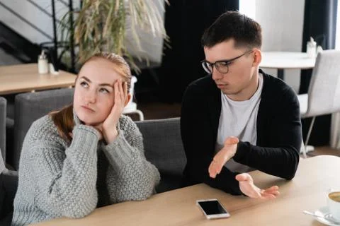 Annoyed man trying to explain something to his wife sitting on a couch in the Foto stock