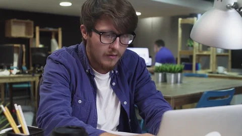 Annoyed programmer with glasses working on laptop in office Stock Footage 129911797
