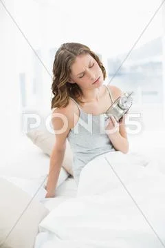 Annoyed slender woman sitting on her bed under the cover Stock Photos