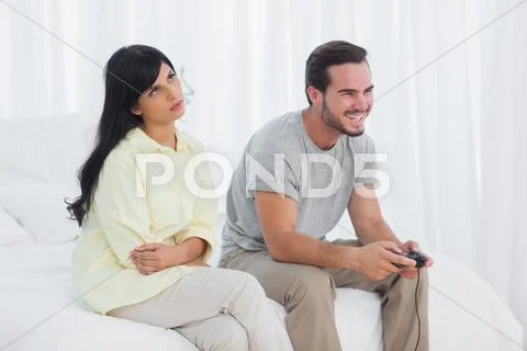 Annoyed woman looking up during her boyfriend playing video games Stock Photos
