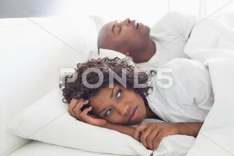Annoyed woman lying in bed with snoring boyfriend Stock Photos