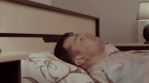 Annoyed young man lying in bed gets tired of noise and covers fully with blanket Stockbeeldmateriaal 68421324