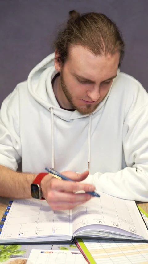 Annoyed young man reading and writing in organizer Stock Footage 239435155