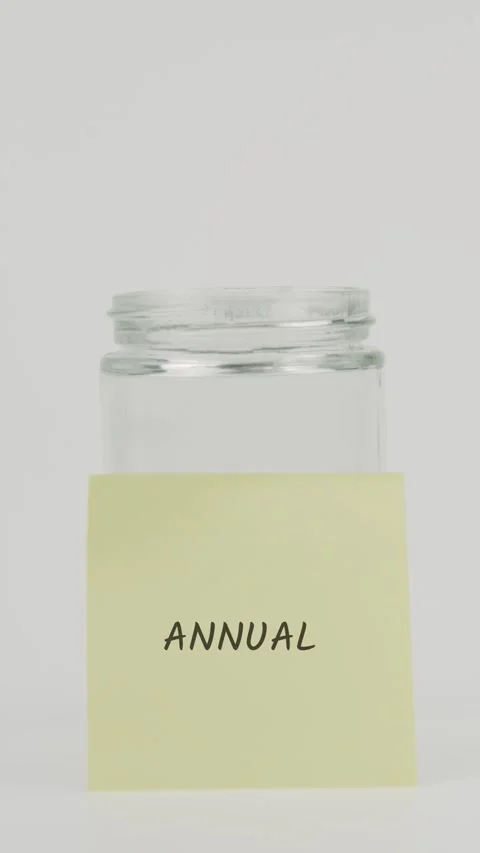 Annual text or word on yellow sticky note attached to glass jar with hand Stock Footage 311677293