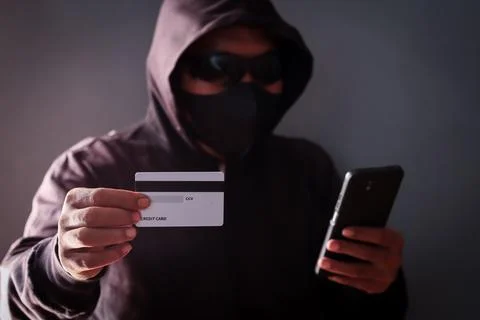 Anonymous cybercriminal using a smartphone and credit Stock Photos