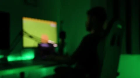 Anonymous gamer sits at gaming PC in green low light room, blurred silhouette Stock Footage 344323871