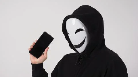 Anonymous hacker and face mask with smartphone in hand. Stock Photos
