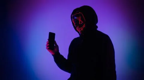 Anonymous hacker and face mask with smartphone in hand. Stock Photos