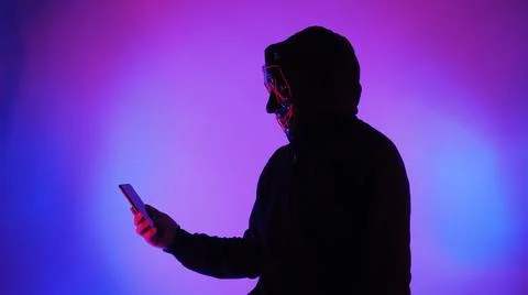 Anonymous hacker and face mask with smartphone in hand. Stockfoto's
