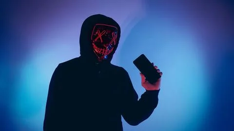 Anonymous hacker and face mask with smartphone in hand. Stockfoto's
