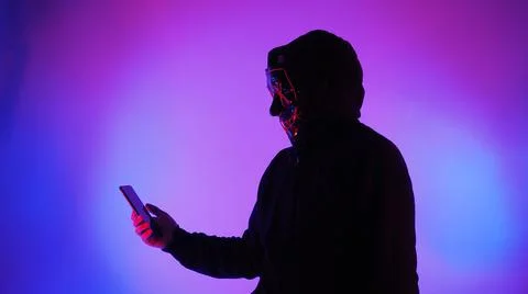 Anonymous hacker and face mask with smartphone in hand. Stock Photos