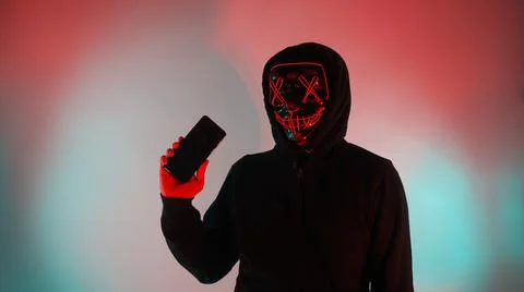 Anonymous hacker and face mask with smartphone in hand. Stock Photos
