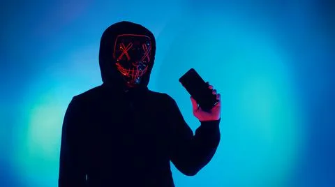 Anonymous hacker and face mask with smartphone in hand. Stock Photos
