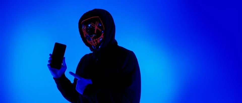 Anonymous hacker and face mask with smartphone in hand. Stockfoto's