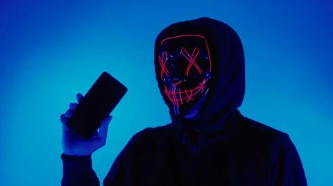 Anonymous hacker and face mask with smartphone in hand. Stock Photos