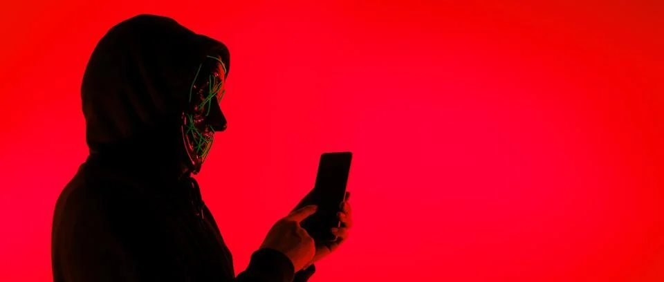 Anonymous hacker and face mask with smartphone in hand. Stockfoto's