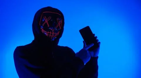 Anonymous hacker and face mask with smartphone in hand. Stockfoto's