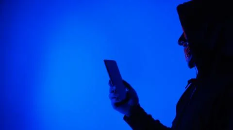 Anonymous hacker and face mask with smartphone in hand. Stockfoto's