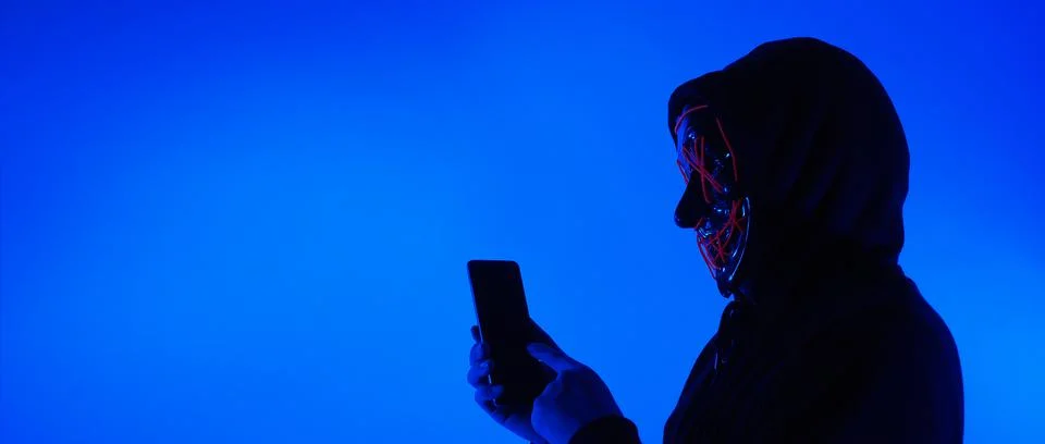 Anonymous hacker and face mask with smartphone in hand. Stockfoto's