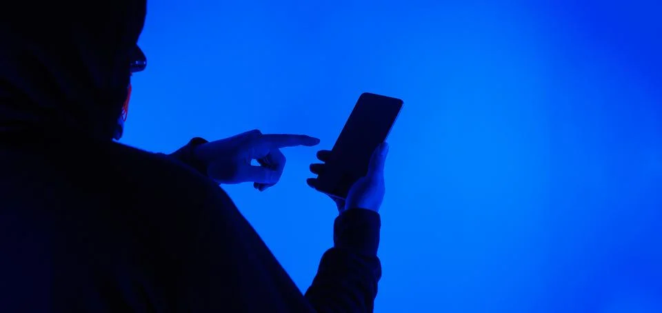 Anonymous hacker and face mask with smartphone in hand. Stockfoto's