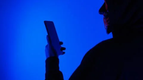 Anonymous hacker and face mask with smartphone in hand. Stockfoto's