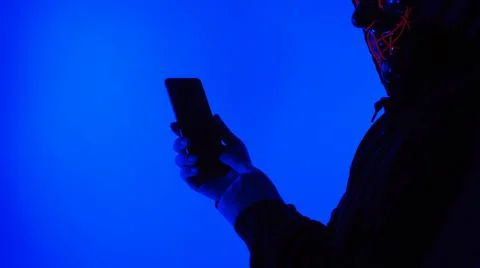 Anonymous hacker and face mask with smartphone in hand. Stockfoto's