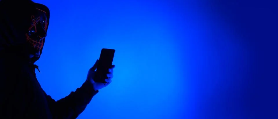 Anonymous hacker and face mask with smartphone in hand. Stockfoto's