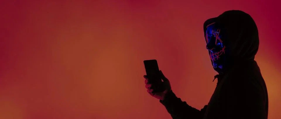 Anonymous hacker and face mask with smartphone in hand. Stockfoto's