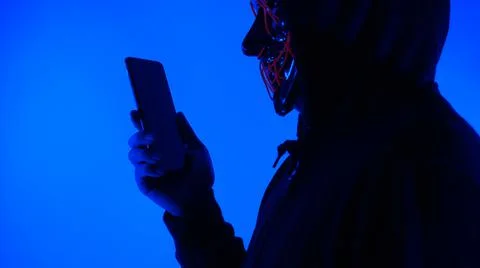 Anonymous hacker and face mask with smartphone in hand. Stock Photos
