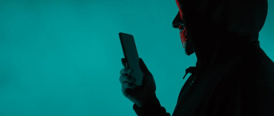 Anonymous hacker and face mask with smartphone in hand. Foto stock