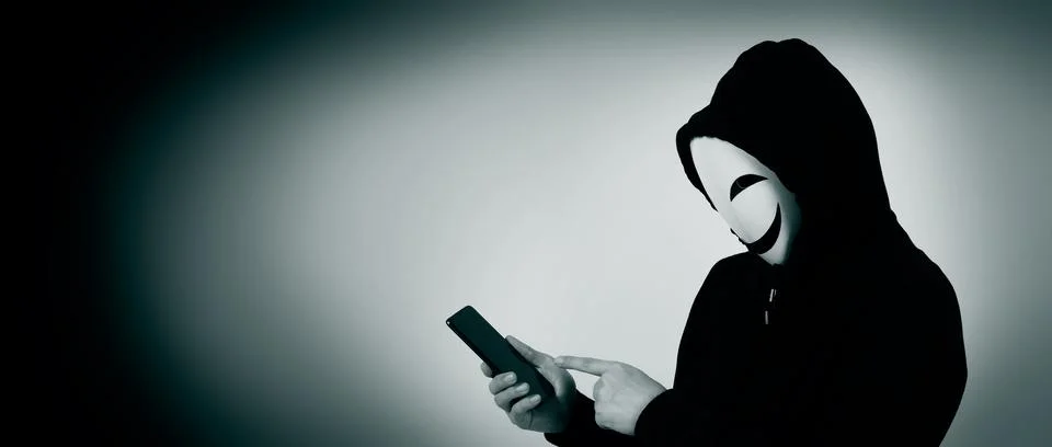 Anonymous hacker and face mask with smartphone in hand. Stock Photos