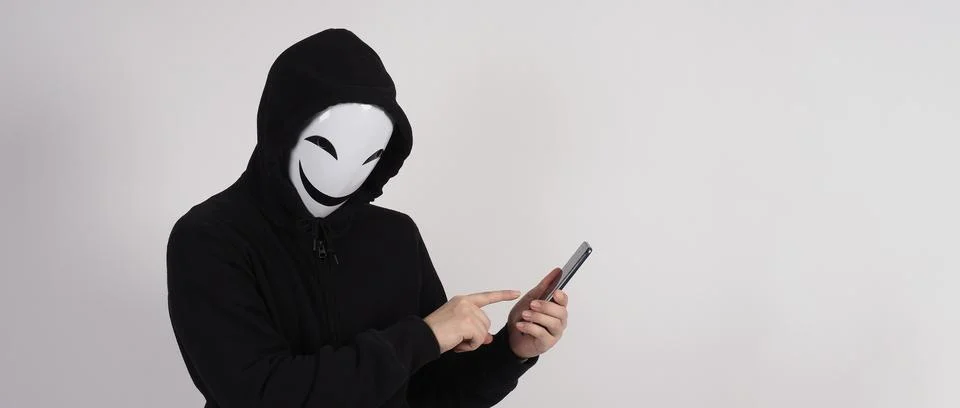 Anonymous hacker and face mask with smartphone in hand. Stock Photos