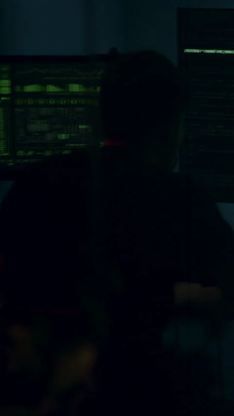 Anonymous hacker from behind in front of several monitors that keep secret Stock Footage 313926851