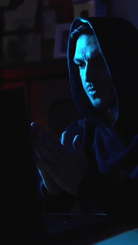 Anonymous hacker browsing the dark web on laptop in dimly lit room symbolizing Stock Footage 310357133