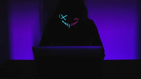Anonymous hacker coding and looks around in police flashing lights. Shaking Stock Footage 170608322
