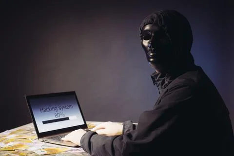 Anonymous hacker programmer uses a laptop to hack the system in the dark. C.. Stock Photos