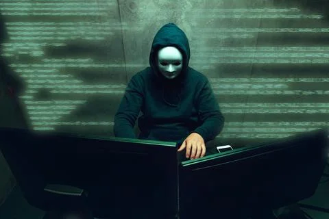 Anonymous hacker wearing face mask working on computer in dark room Stock Photos
