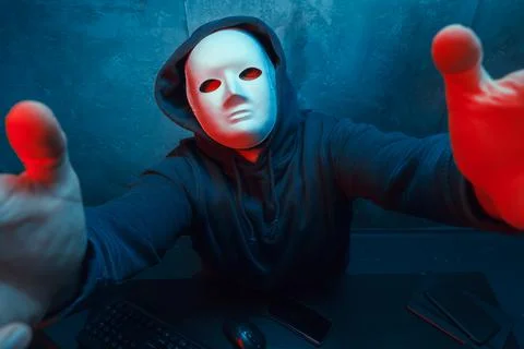 Anonymous hacker wearing face mask working on computer in dark room Stock Photos