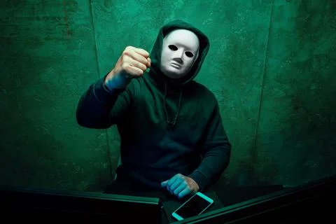 Anonymous hacker wearing face mask working on computer in dark room Stock Photos
