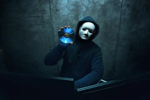 Anonymous hacker wearing face mask working on computer in dark room Stock Photos
