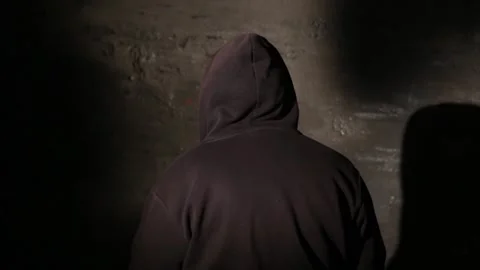 Anonymous hooded hacker with back to camera during police interrogation in .. Stock Footage 320622631